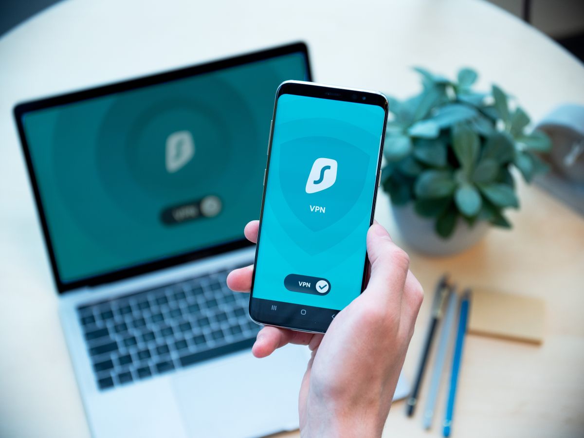 노트북을 배경으로 VPN 보안 앱이 켜진 스마트폰을 든 손